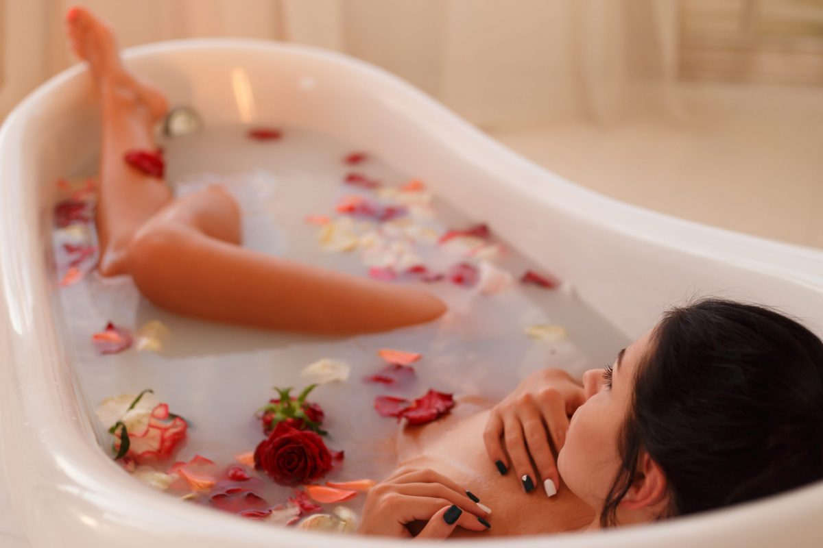 Attractive girl takes a bath with milk and rose petals. Spa treatments for skin rejuvenation