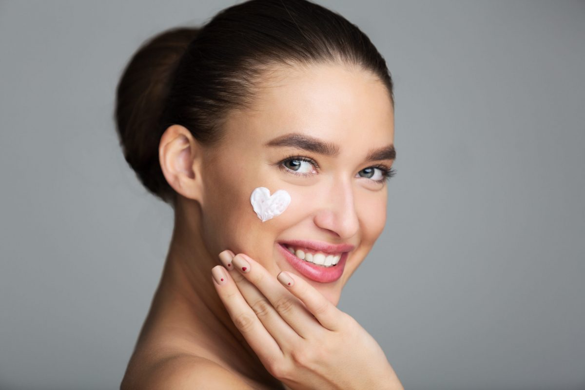 Beauty Skin Care. Cream In Heart Shape On Female Cheek, Grey Studio Background