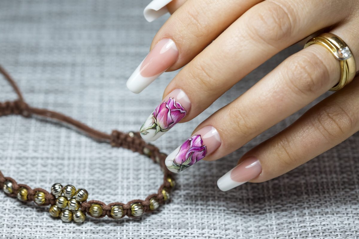 Beautiful multicolored flowers on a transparent lacquer on the nails on a gray decor
